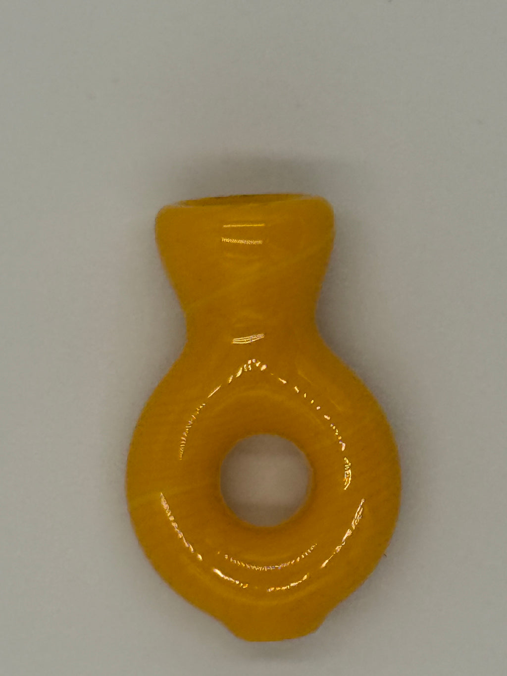 A small glossy yellow glass ring-shaped pipe with a central hole and a short cylindrical extension on the left, shown on a plain light gray background.