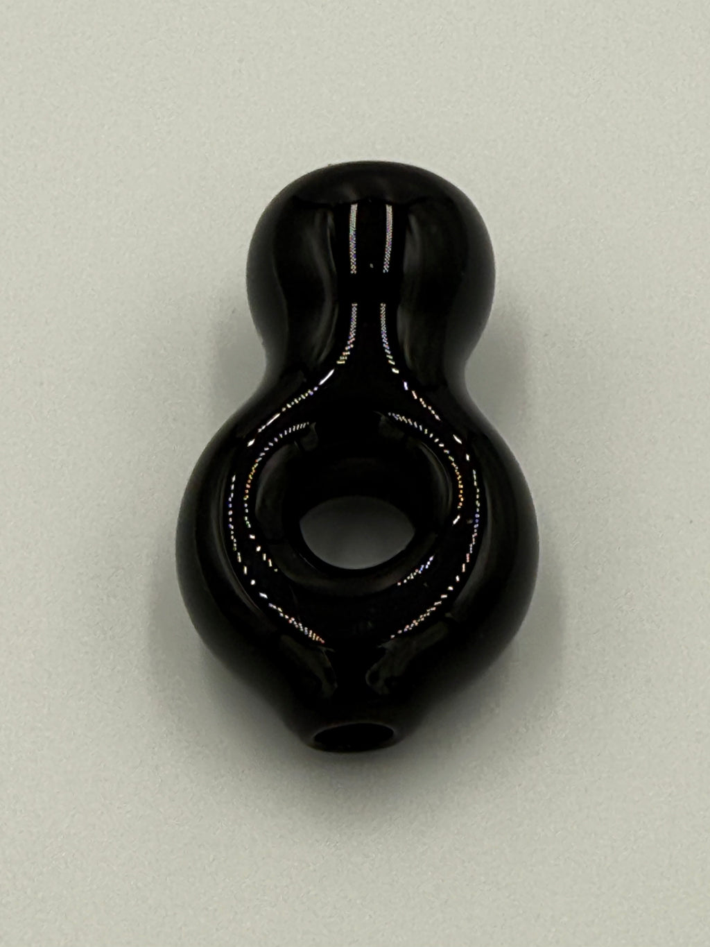 A glossy black glass pipe with a bulbous body and a central hole, photographed on a light gray background.