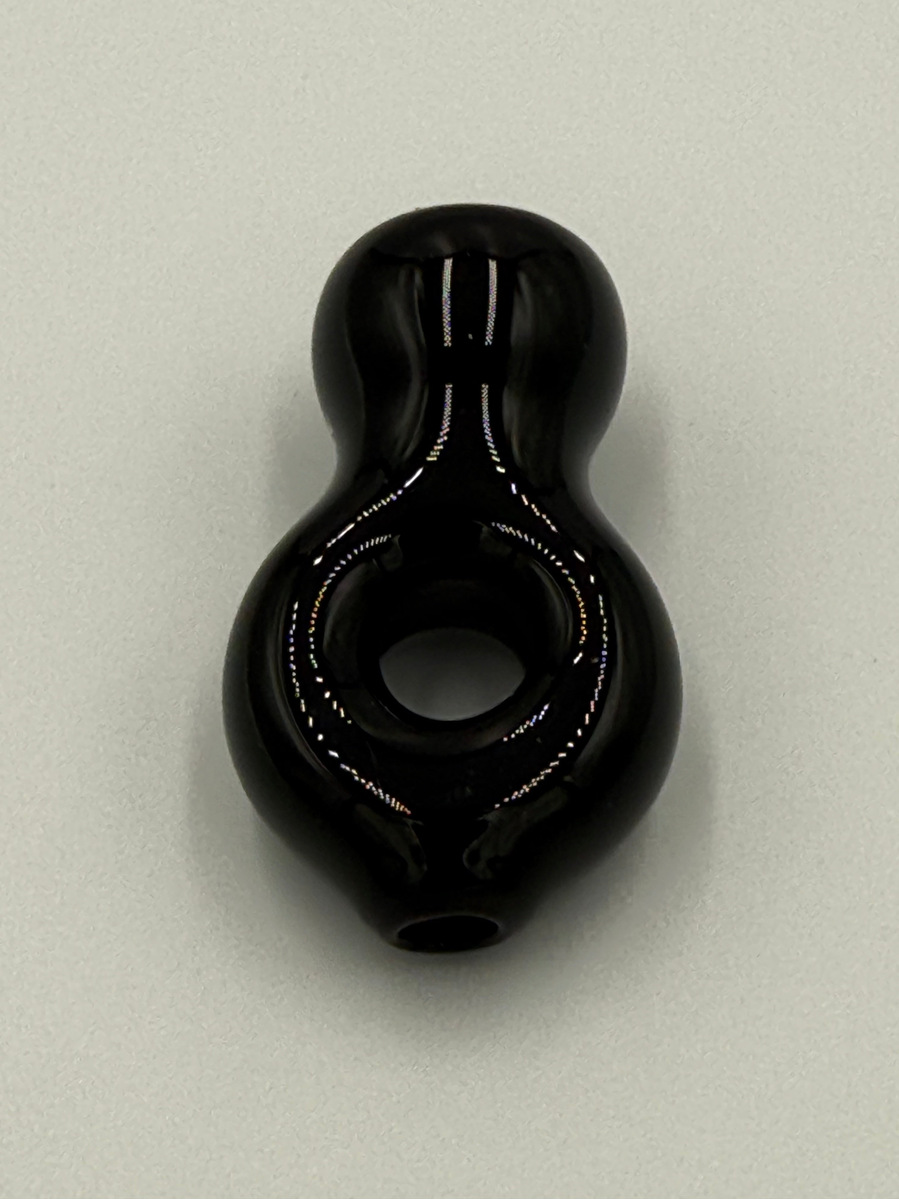 A glossy black glass pipe with a bulbous body and a central hole, photographed on a light gray background.