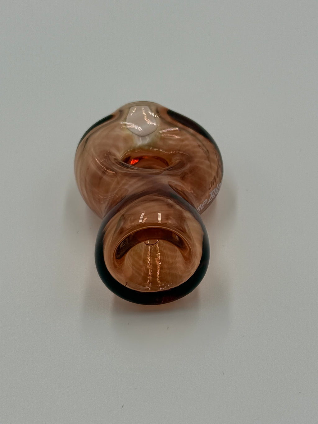 A small hand-blown glass object with a warm amber-brown body, dark rim, and a clear faceted section, photographed on a plain light background.
