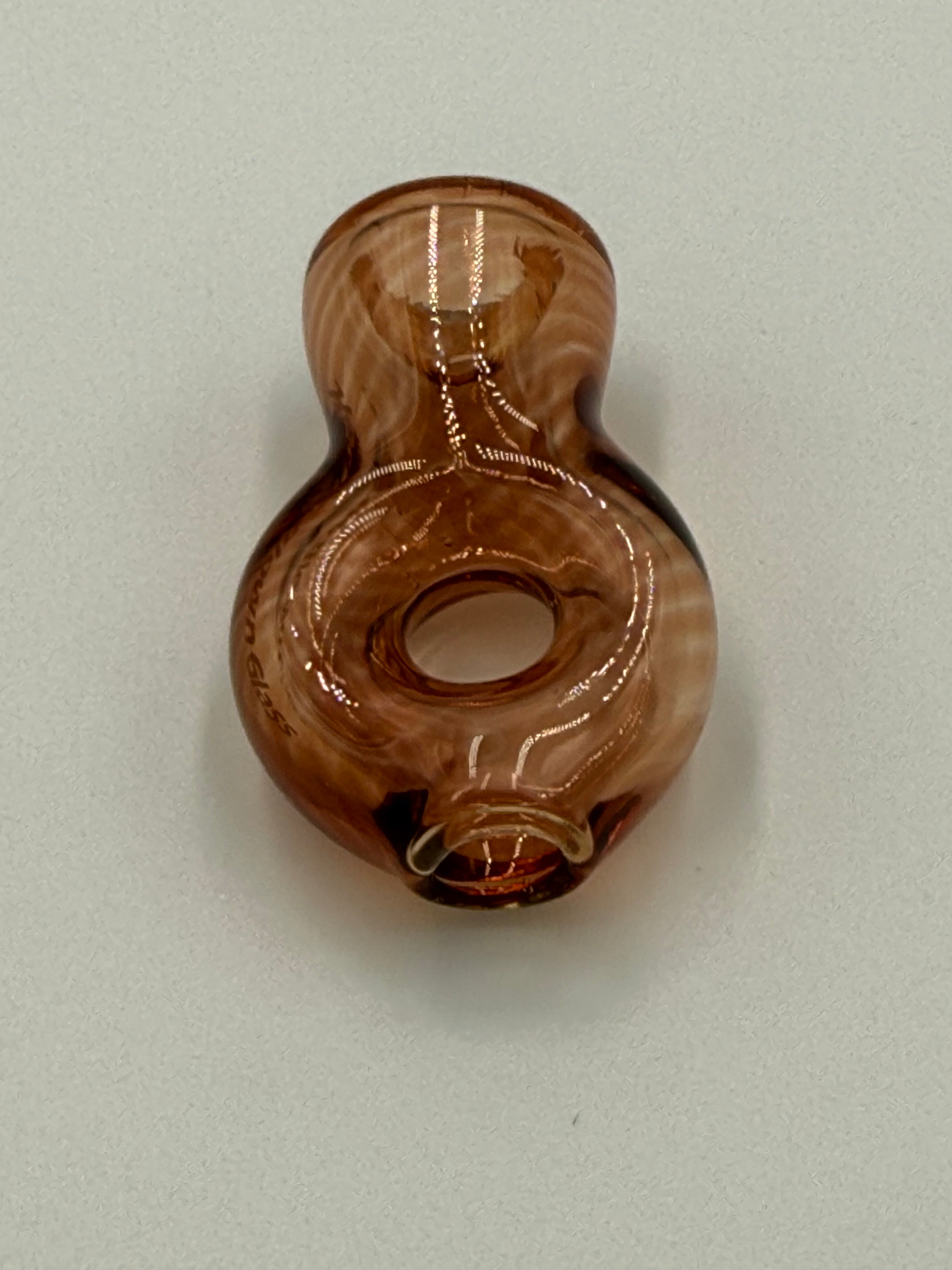 A small hand-blown glass object with a bulbous shape, featuring a brown and amber marbled pattern, photographed on a neutral light gray background.