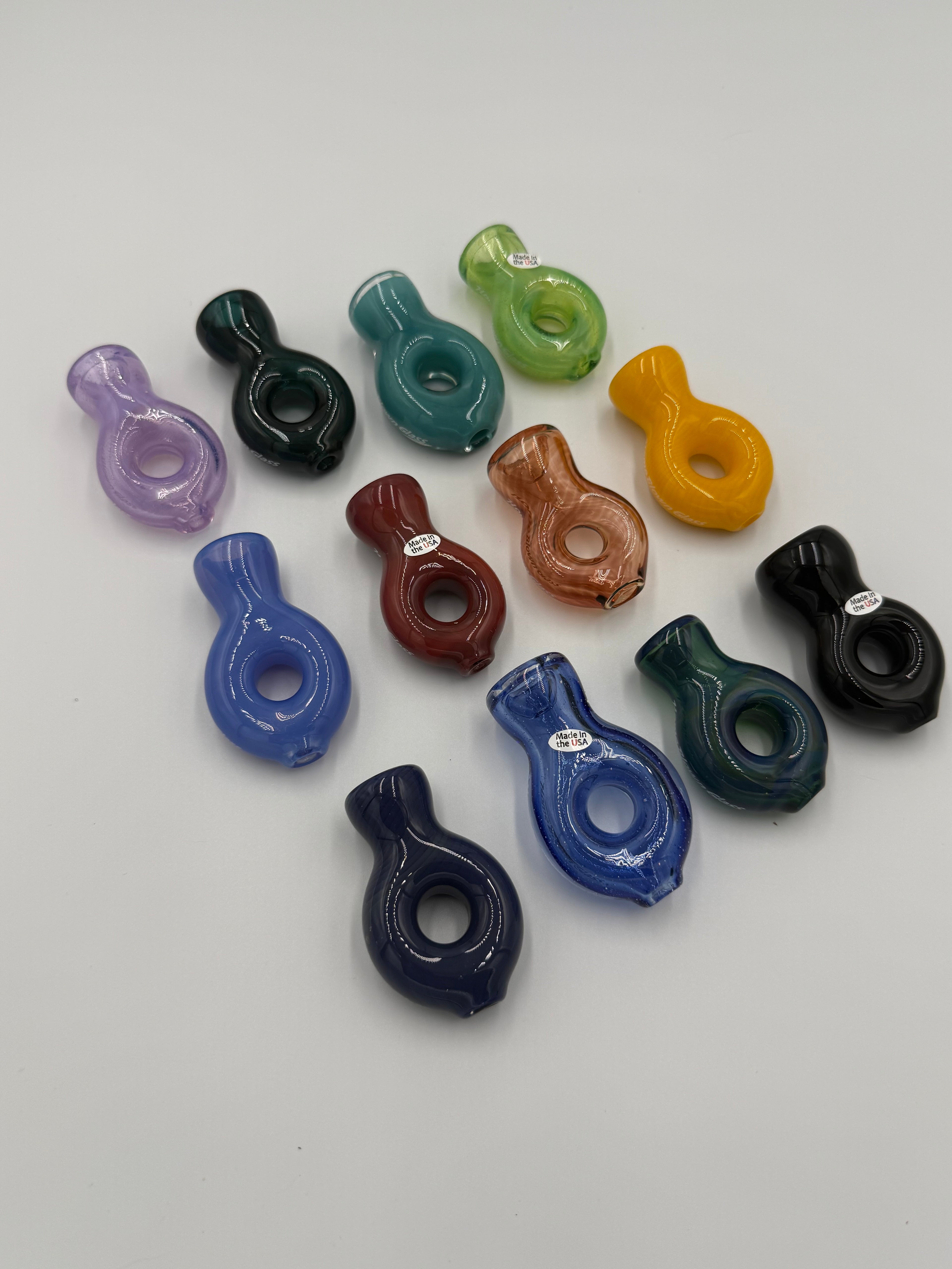 A set of twelve small, glossy, bottle-shaped glass pipe pieces in various colors, arranged on a plain light gray background.